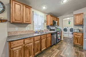 Kitchen featuring stainless steel appliances, a sink, washing machine and dryer, dark countertops, and dark wood-type flooring