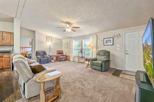 Living room featuring a ceiling fan, dark colored carpet, and a textured ceiling