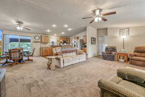 Living room featuring vaulted ceiling, light carpet, and ceiling fan