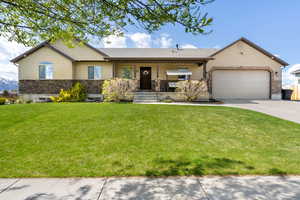 Ranch/rambler home featuring a garage, stone siding, a front yard, and concrete driveway