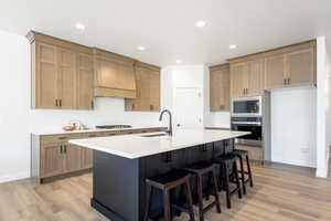 Kitchen featuring stainless steel appliances, custom exhaust hood, a sink, light wood-style floors, and recessed lighting