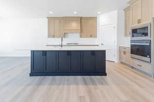 Kitchen with built in microwave, oven, a sink, premium range hood, and light wood-type flooring
