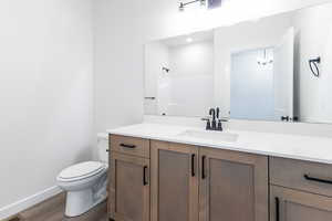 Bathroom with wood finished floors, toilet, vanity, baseboards, and a shower