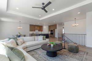 Living room featuring a chandelier, ceiling fan, light wood-style flooring, recessed lighting, and a tray ceiling