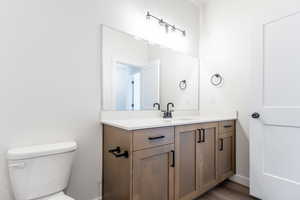 Bathroom featuring vanity, toilet, wood finished floors, and baseboards