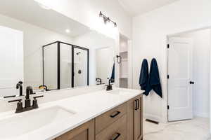 Bathroom with a shower stall, double vanity, marble finish floors, and baseboards