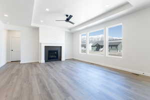 Unfurnished living room featuring ceiling fan, light wood-style flooring, a fireplace, and a raised ceiling