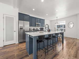 Kitchen featuring stainless steel appliances, a kitchen breakfast bar, recessed lighting, a chandelier, and wood finished floors