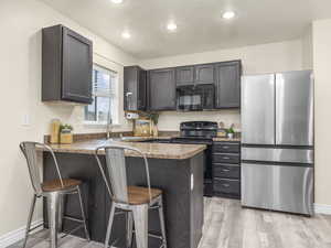 Kitchen with a sink, black appliances, a peninsula, light wood-style flooring, and a breakfast bar area