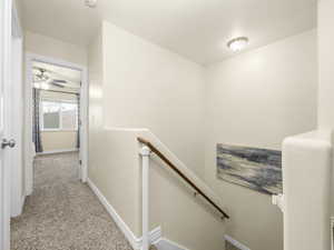 Corridor with baseboards, light colored carpet, and an upstairs landing