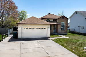 Traditional-style house featuring brick siding, concrete driveway, a front lawn, fence, and roof with shingles