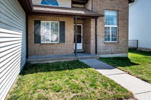 Property entrance featuring a lawn, brick siding, and a shingled roof