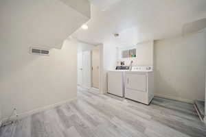 Laundry area featuring baseboards, light wood-type flooring, visible vents, and independent washer and dryer