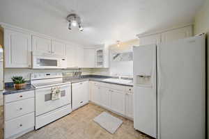 Kitchen with a sink, dark countertops, white cabinetry, glass insert cabinets, and white appliances