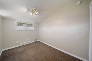 Carpeted empty room with vaulted ceiling, visible vents, and baseboards