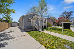 Bungalow-style house with a pergola, a detached garage, concrete driveway, a front lawn, and an outdoor structure