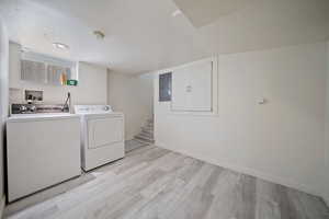 Laundry room featuring electric panel, light wood-type flooring, baseboards, independent washer and dryer, and laundry area