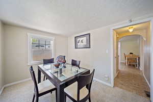 Dining room featuring baseboards, arched walkways, a textured ceiling, and light colored carpet