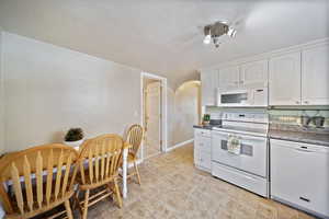 Kitchen featuring white cabinets, dark countertops, white appliances, and arched walkways