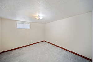 Below grade area featuring a textured ceiling, carpet flooring, and baseboards
