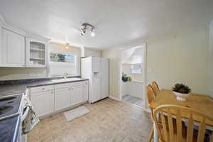 Kitchen featuring a sink, dark countertops, white cabinetry, electric range oven, and white fridge with ice dispenser