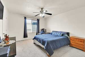 Carpeted bedroom with ceiling fan, baseboards, and a textured ceiling