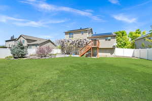 Rear view of house featuring stairway, roof mounted solar panels, a fenced backyard, a yard, and a wooden deck