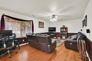 Living room featuring a ceiling fan, visible vents, a wainscoted wall, and light wood-style flooring