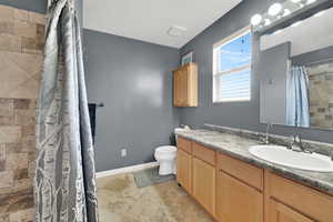 Bathroom featuring a textured ceiling, toilet, stone tile floors, a tile shower, and vanity