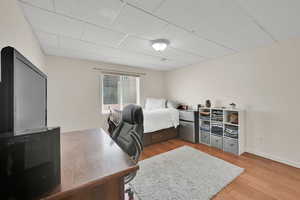 Bedroom featuring freestanding refrigerator, wood finished floors, and a drop ceiling