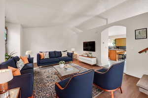 Living room featuring lofted ceiling, baseboards, wood finished floors, and arched walkways