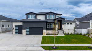 View of front of house featuring concrete driveway, a front lawn, stone siding, fence, and a garage