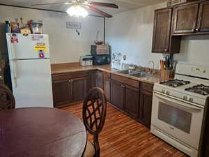 Kitchen with dark brown cabinets, wood finished floors, a sink, white appliances, and ceiling fan
