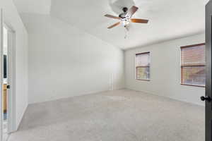 Spare room featuring baseboards, lofted ceiling, a ceiling fan, and light carpet