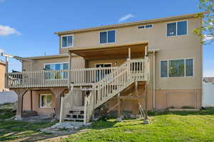 Rear view of property with stucco siding, a deck, stairs, and a lawn