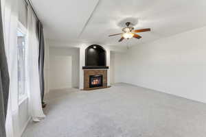 Unfurnished living room with a fireplace, baseboards, carpet floors, and ceiling fan
