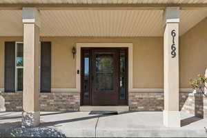 Doorway to property featuring stucco siding, brick siding, and a porch