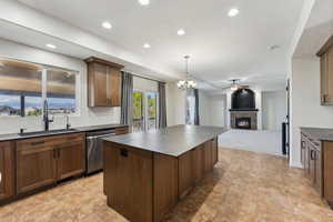 Kitchen featuring dark countertops, dishwasher, a sink, a center island, and a fireplace