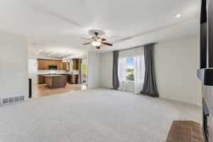Unfurnished living room with recessed lighting, visible vents, light carpet, and ceiling fan with notable chandelier