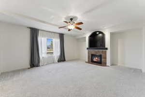 Unfurnished living room featuring a tile fireplace, carpet flooring, a ceiling fan, and baseboards