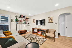 Living area with arched walkways, light wood-style floors, baseboards, and recessed lighting