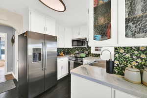 Kitchen featuring a sink, tasteful backsplash, dark wood finished floors, white cabinetry, and appliances with stainless steel finishes