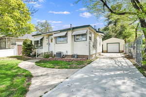 Bungalow-style house with central AC, concrete driveway, fence, an outbuilding, and a garage