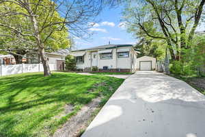 View of front of home featuring a front lawn, a detached garage, concrete driveway, fence, and an outdoor structure