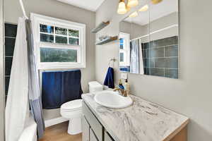 Full bathroom with shower / tub combo, toilet, vanity, and wood finished floors