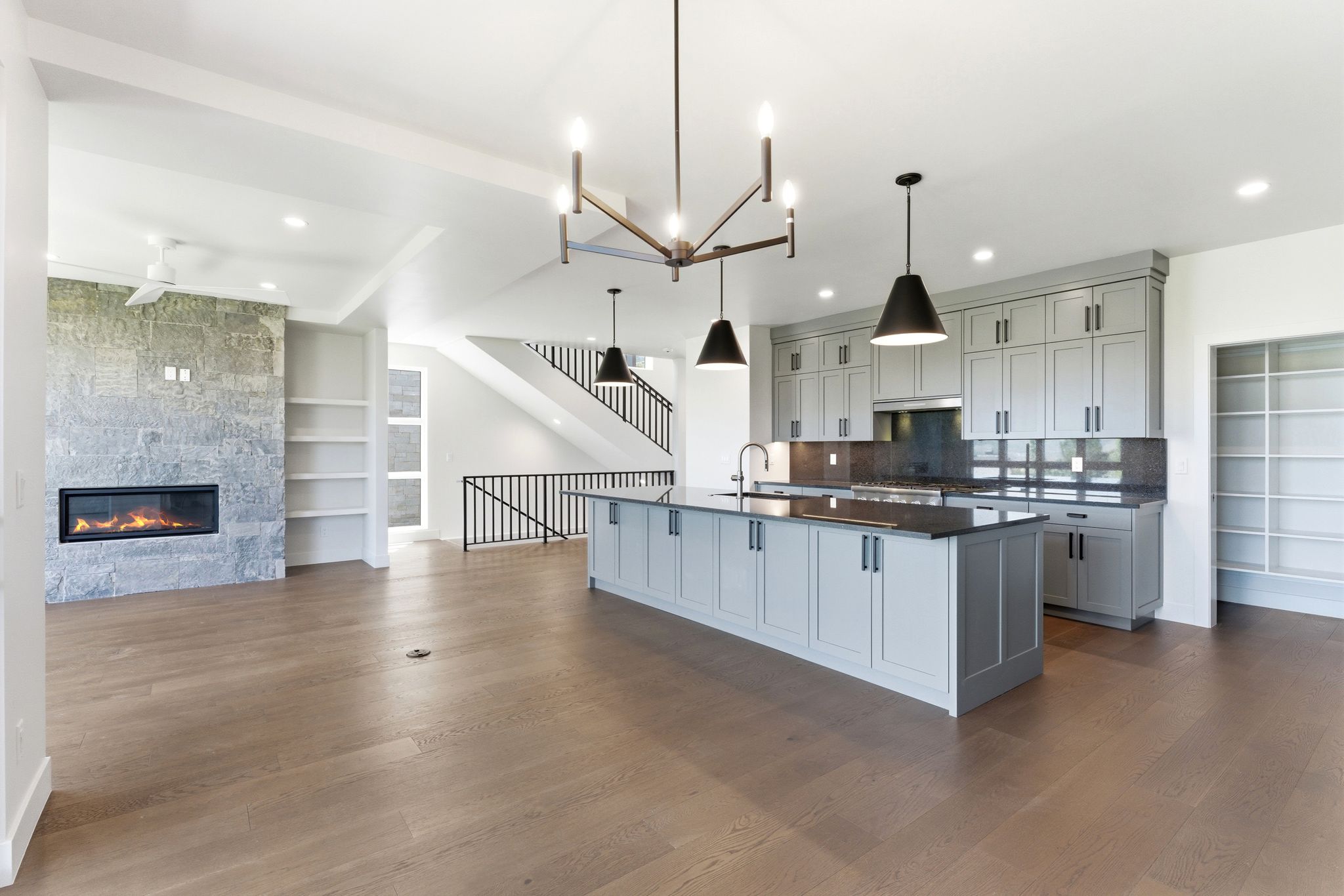 Open-concept living space featuring wood-finish flooring, a contemporary fireplace with a stone surround, and built-in shelving