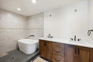 Full bath with double vanity, tile walls, a freestanding bath, light tile patterned flooring, and recessed lighting