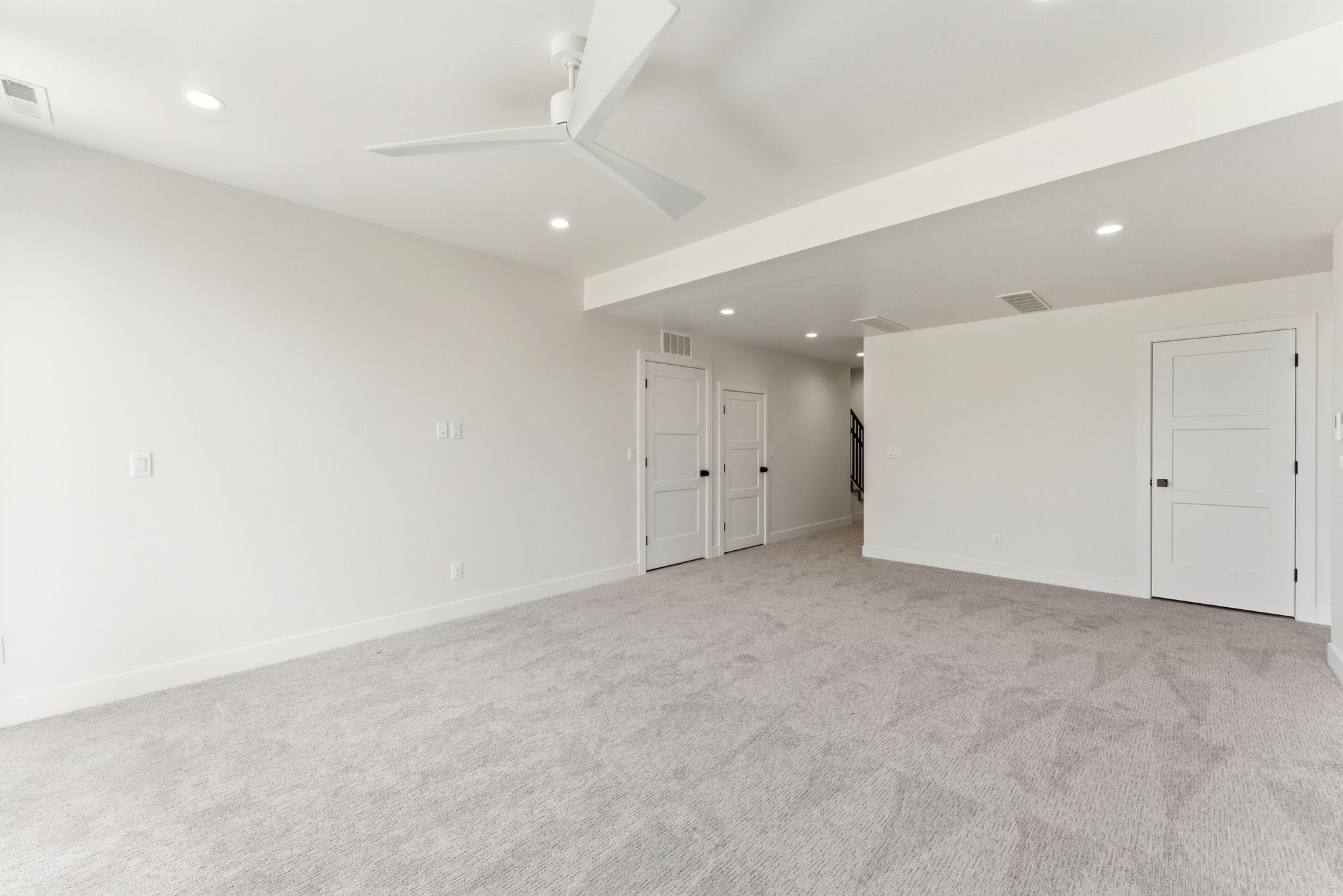 Expansive room featuring light gray carpeting, recessed lighting, white walls, and white three-panel interior doors with matte black hardware