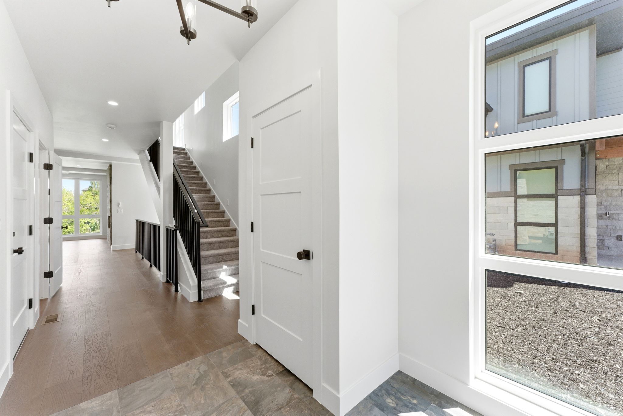 Bright entryway featuring a modern staircase with black iron railing, wood-finish flooring, recessed lighting, and a contemporary chandelier