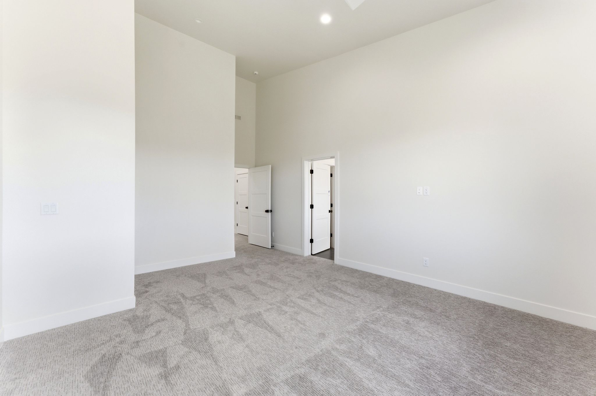 Spacious interior room featuring light gray carpeting, crisp white walls, and a recessed ceiling light